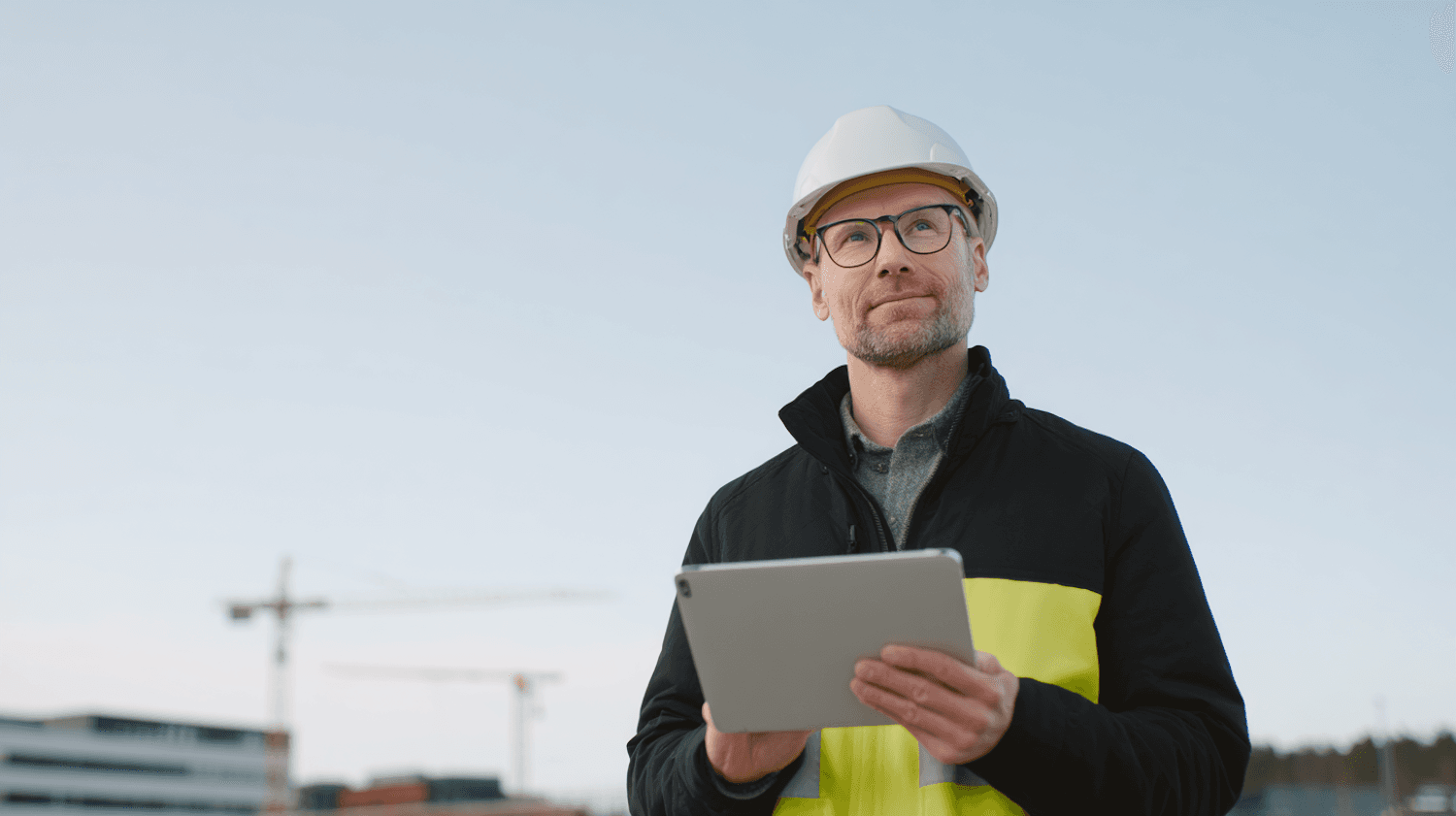 A field technician in a hard hat and safety vest checking jobs on a tablet